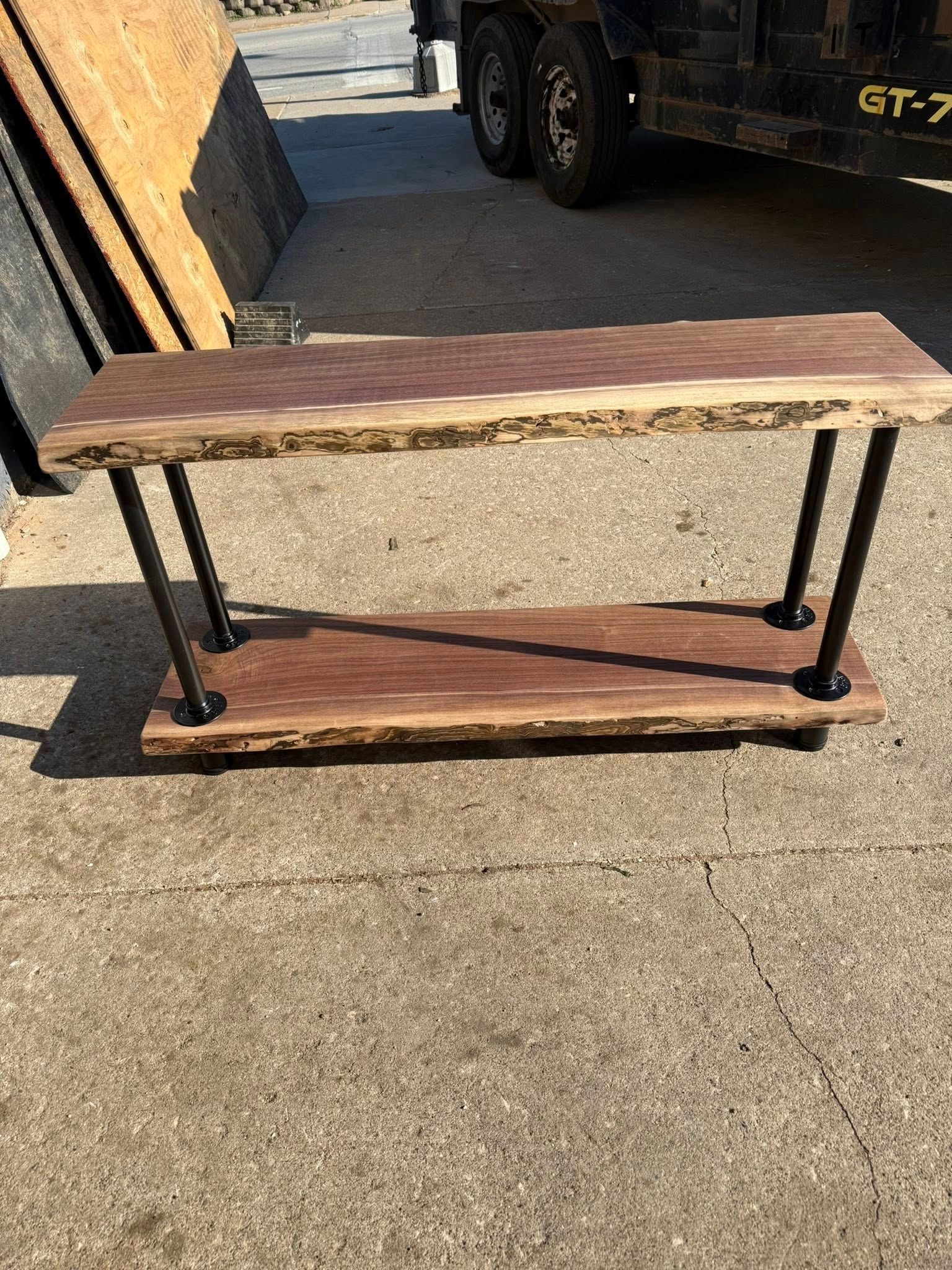 Wooden console table with black metal legs on a sunlit concrete surface outdoors
