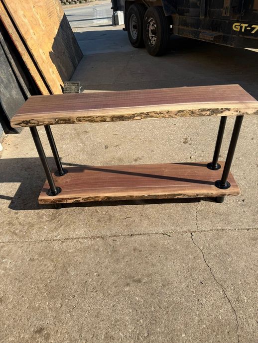 Rustic wooden bench with black metal legs sitting on a concrete surface outdoors.