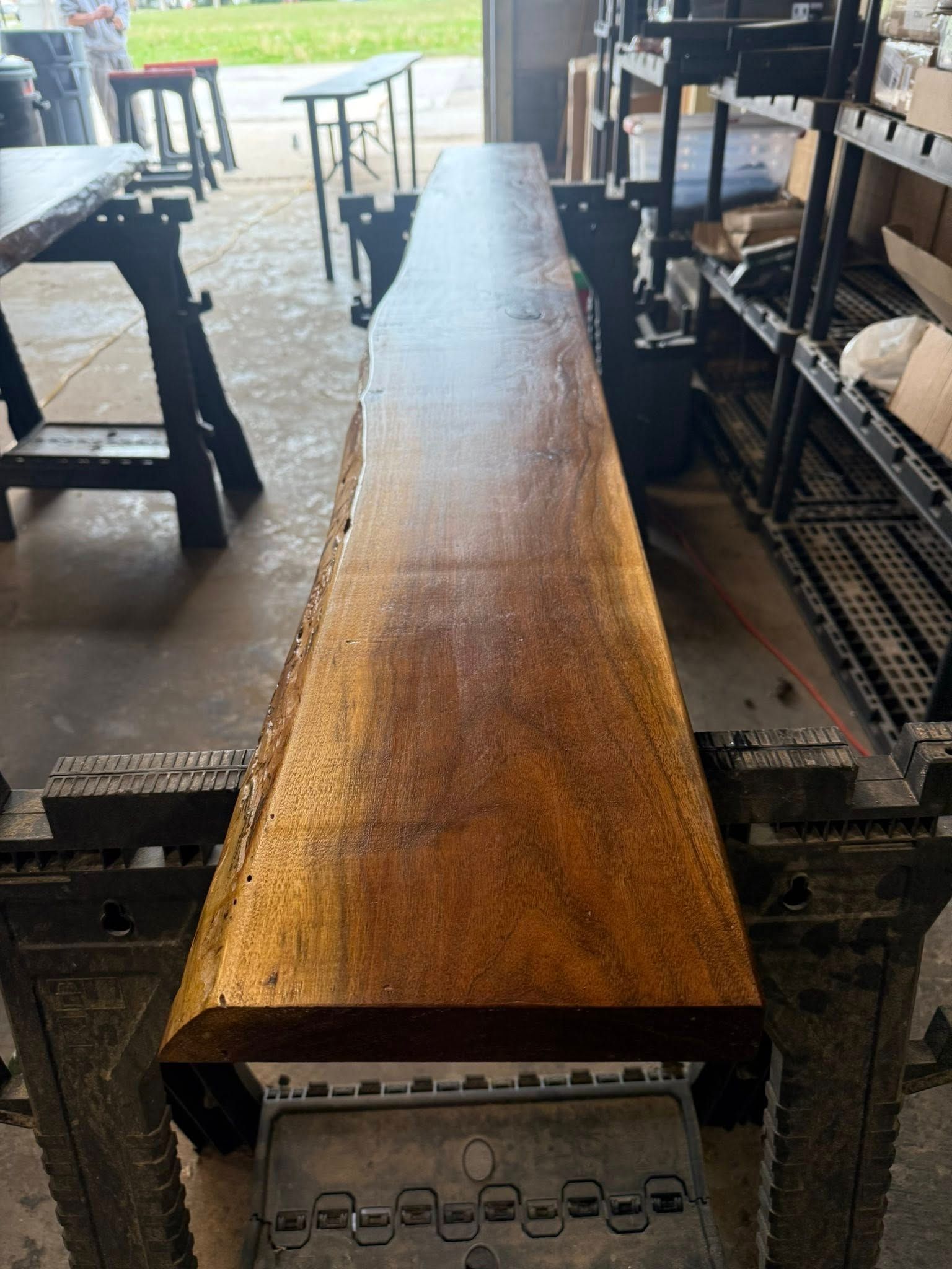 Long wooden plank on a metal worktable in a workshop, with tools and tables in the background