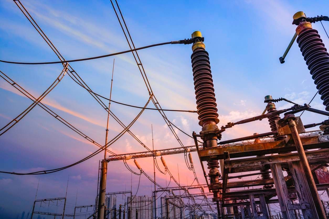Electrical power substation with wires, insulators, and a sunset sky.