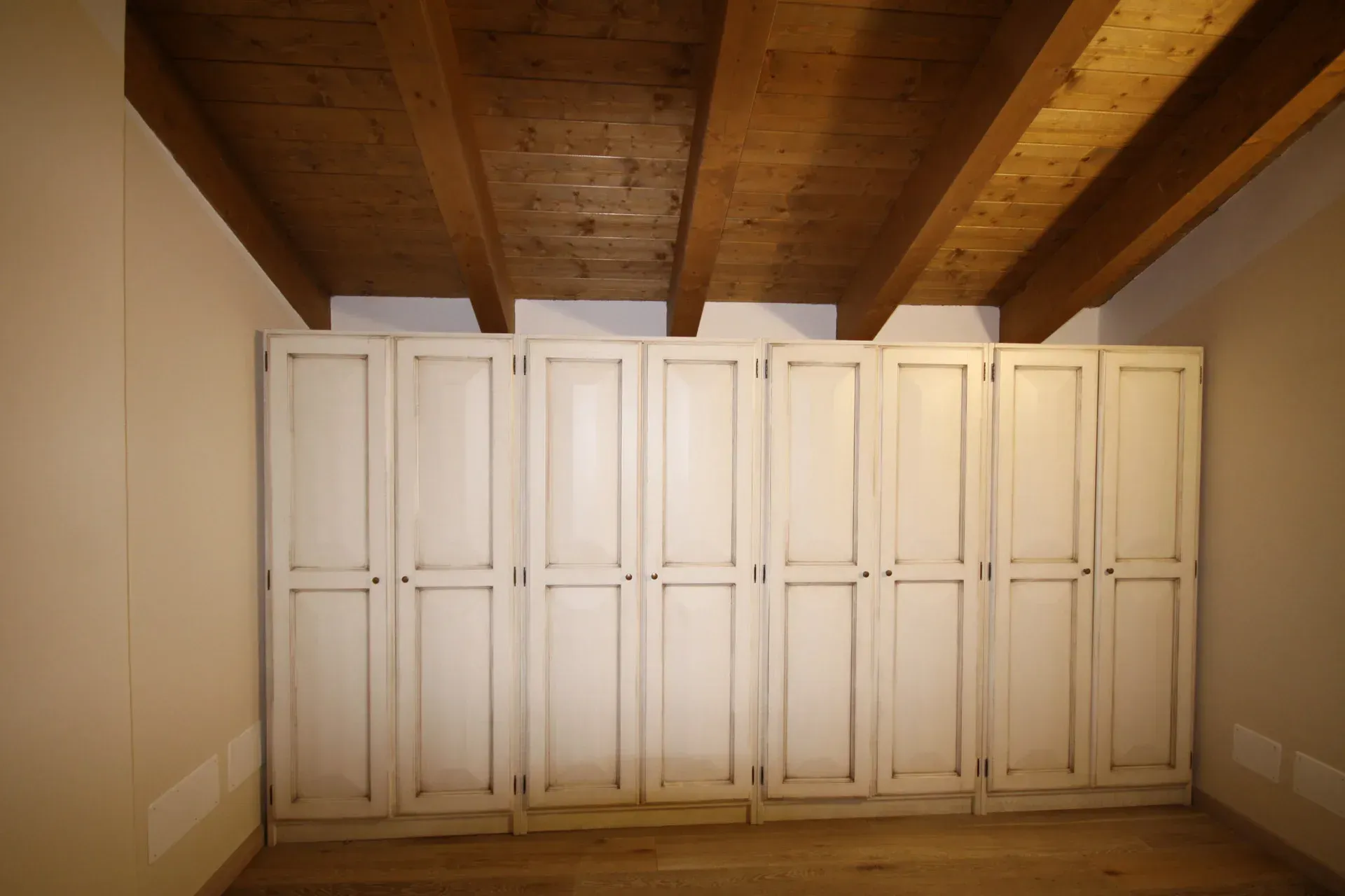 Ante bianche dell'armadio sotto un soffitto con travi in legno.