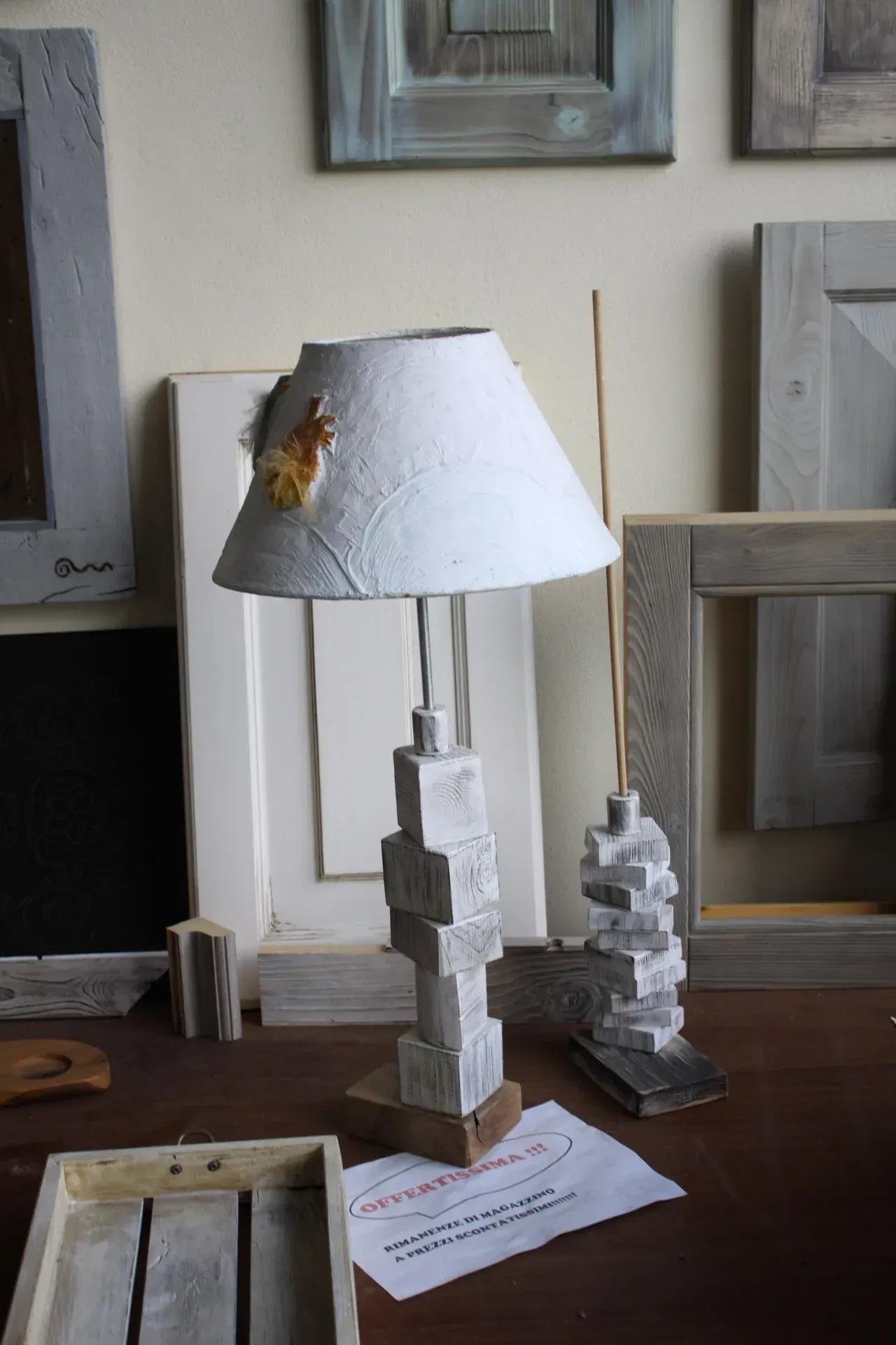 Paralume bianco su base di lampada a blocchi sovrapposti. Sullo sfondo un'opera d'arte con cornice in legno.