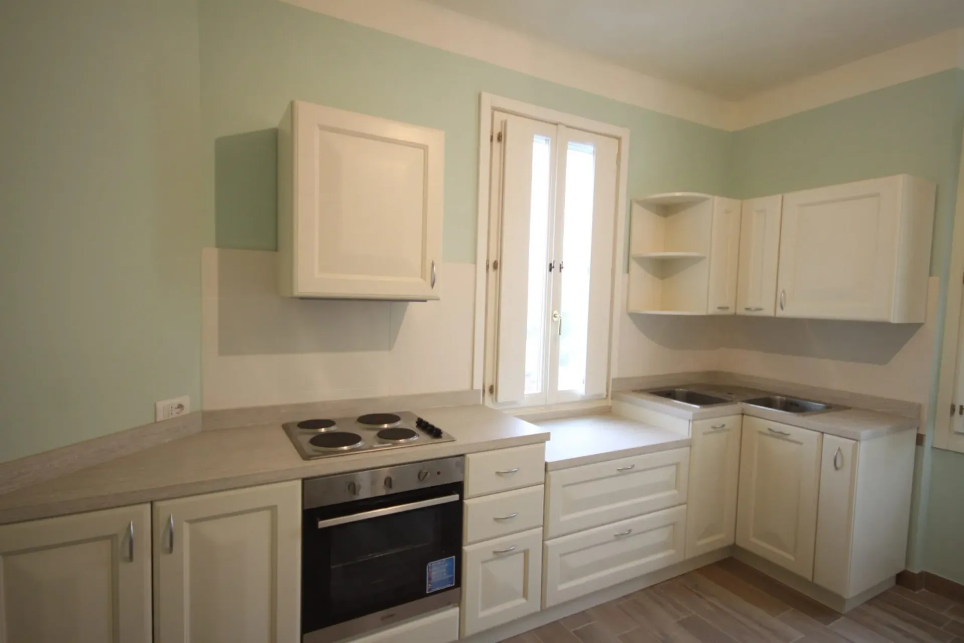 Mobili da cucina ed elettrodomestici bianchi in una stanza con pareti azzurre e una finestra.