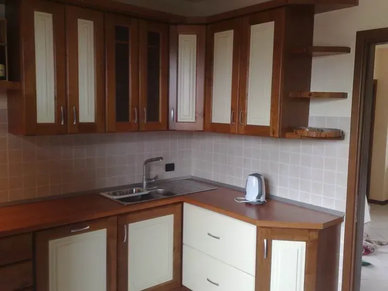 Cucina angolare con mobili in legno marrone e pannelli color crema, lavello in acciaio inossidabile.