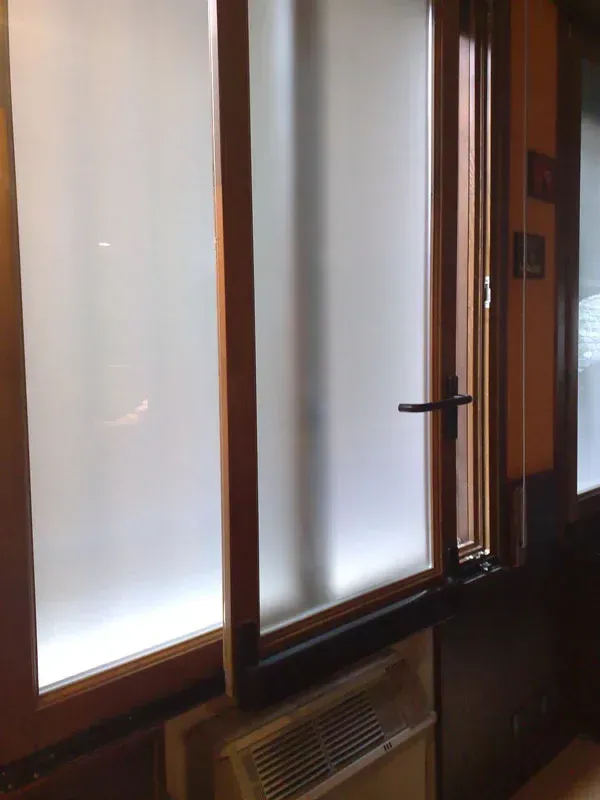 Finestra con vetro smerigliato, cornice in legno e maniglia nera. Sotto c'è un termosifone.