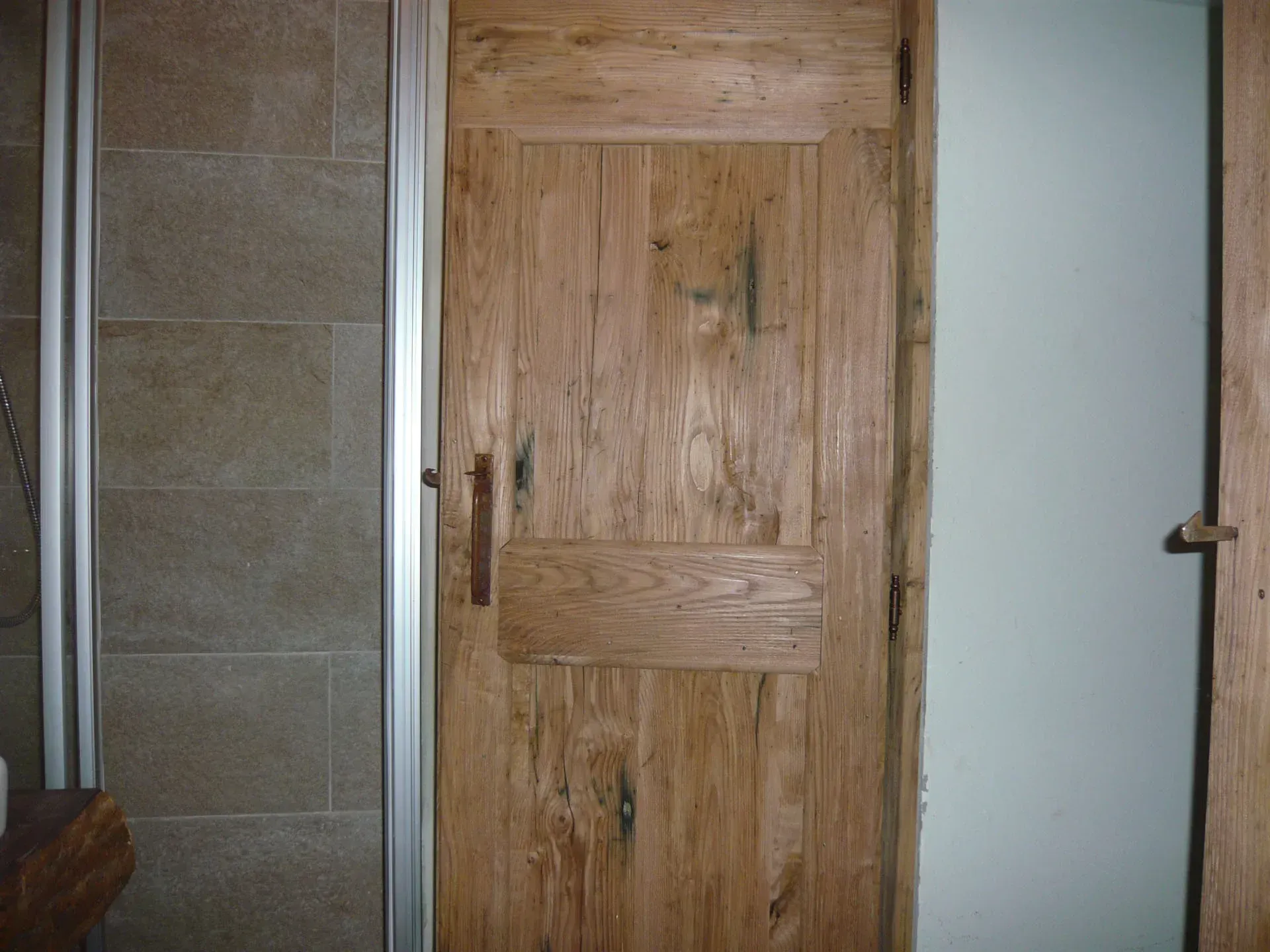 Porta del bagno in legno e doccia accanto a una parete piastrellata beige.
