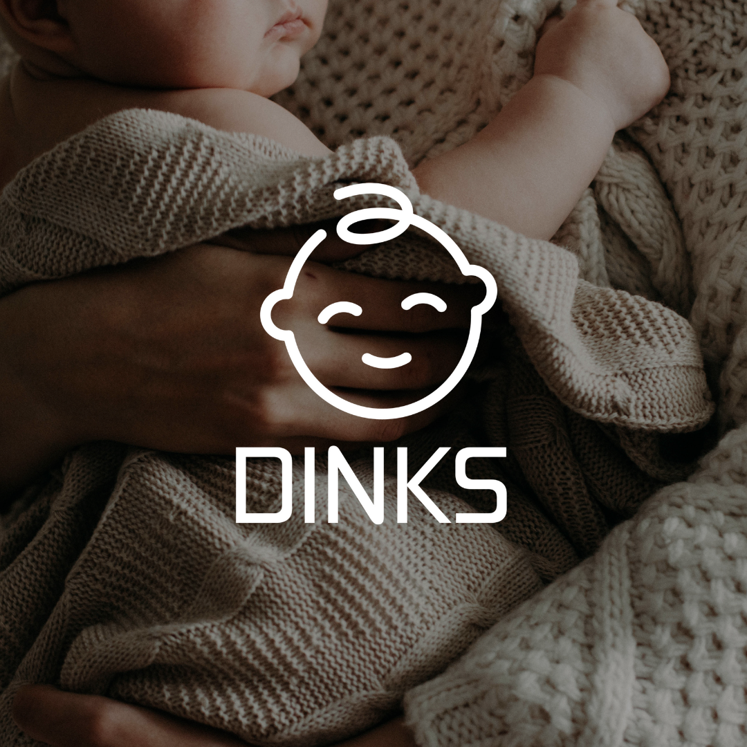 A person is holding a baby wrapped in a blanket with the word dinks below it