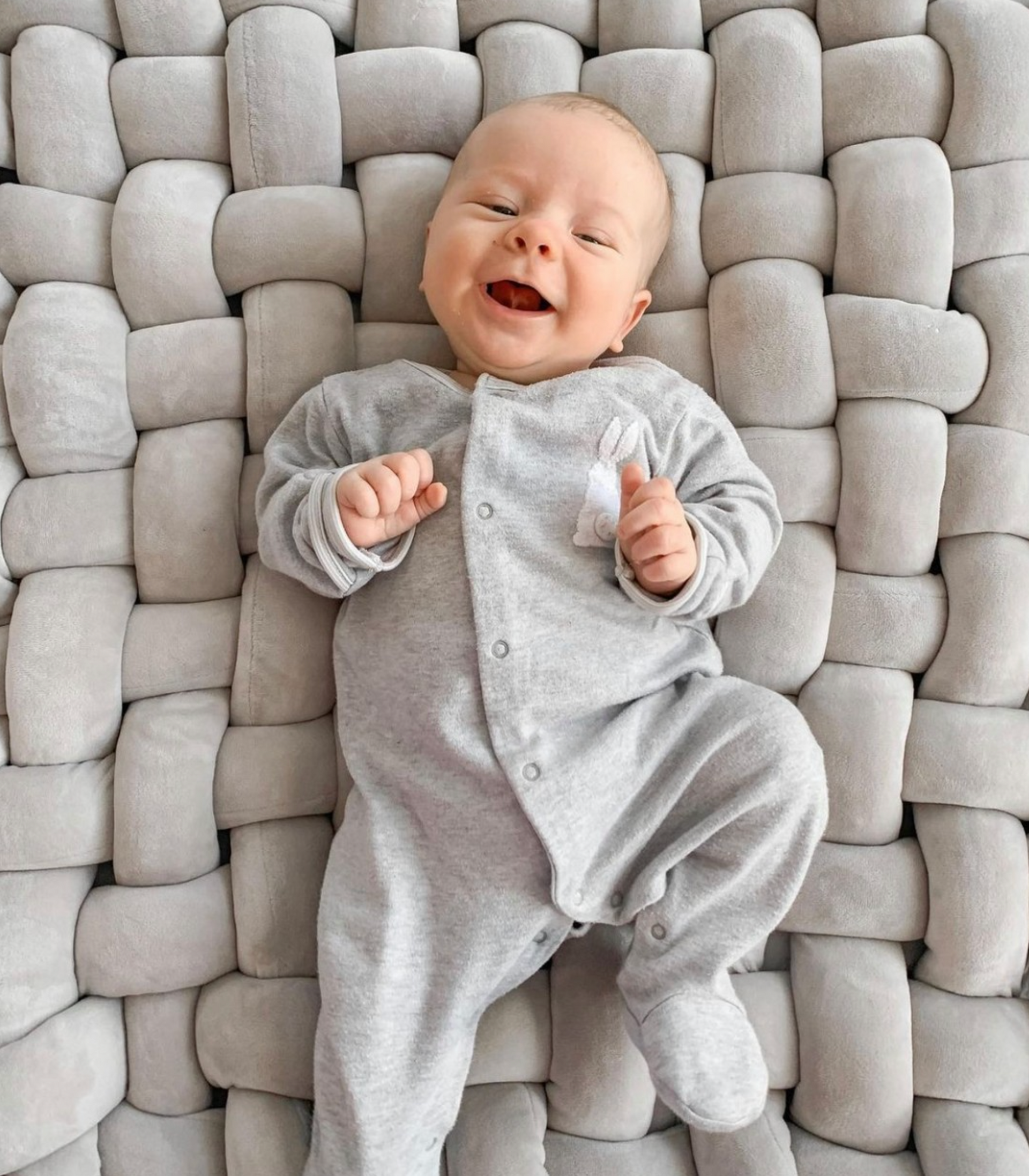 A baby is laying on a blanket and smiling.