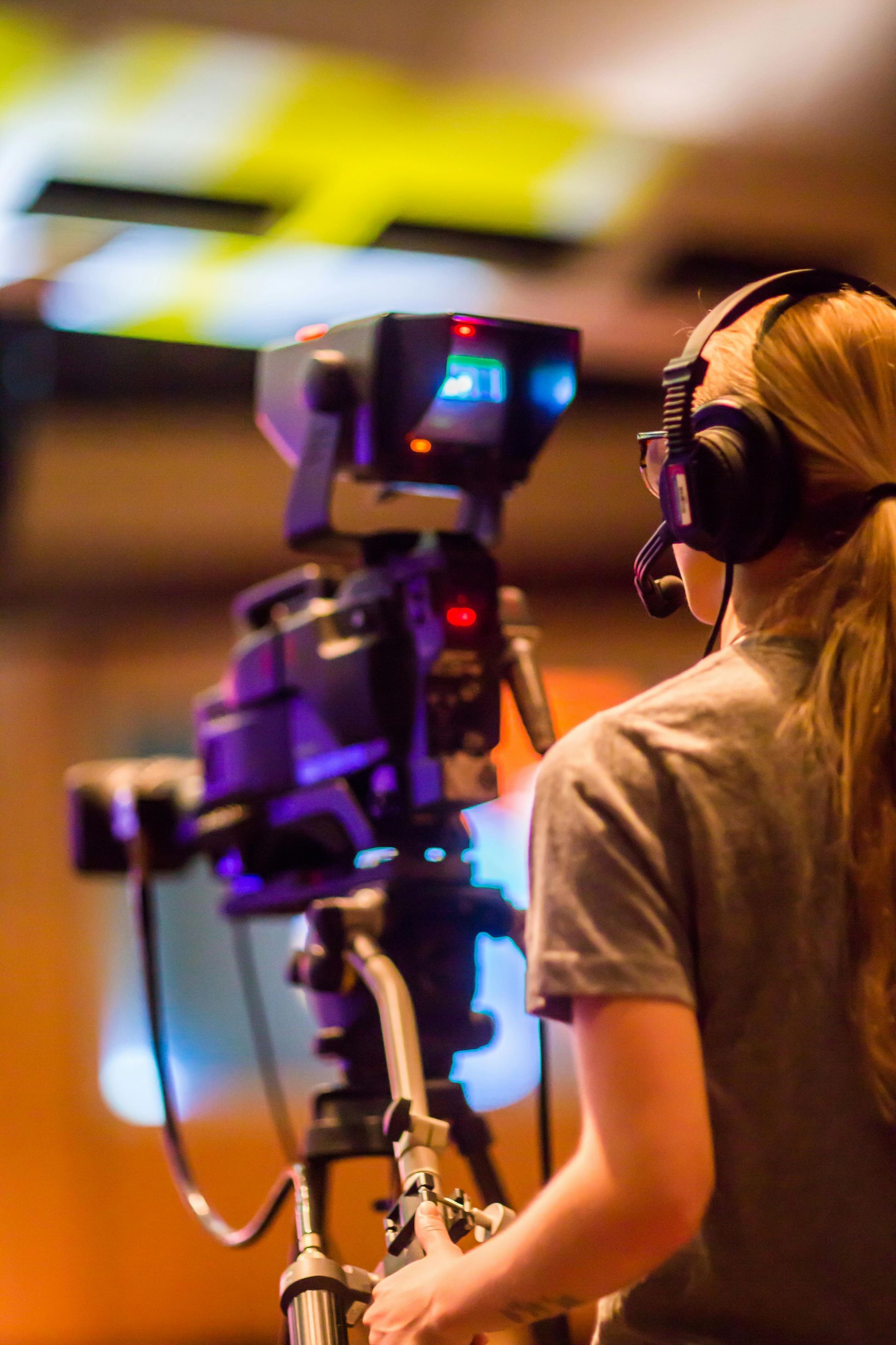 A person with headphones operates a video camera on a tripod, likely in a studio setting.