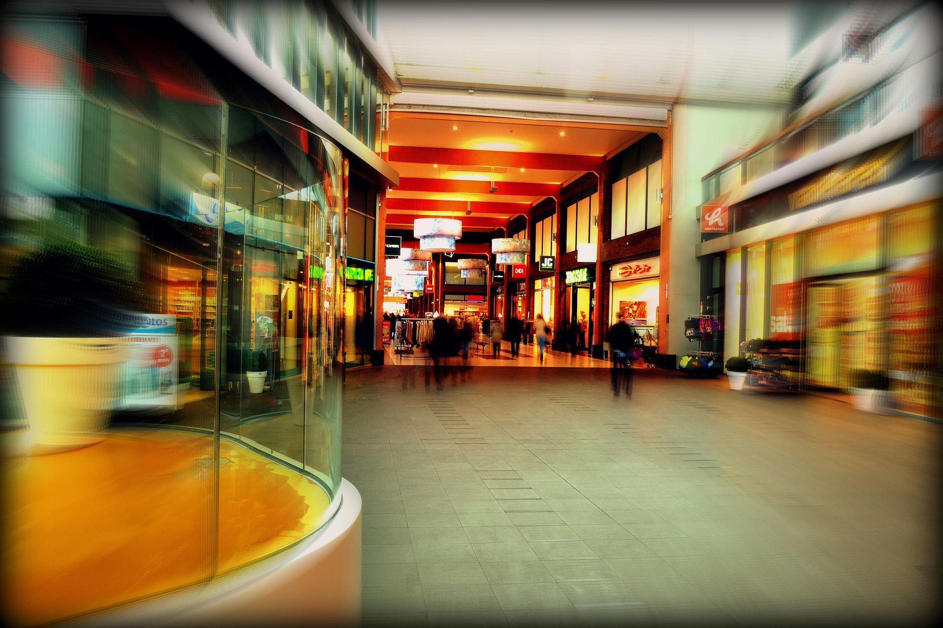 Mall interior with blurred figures walking past storefronts and vibrant orange lighting.
