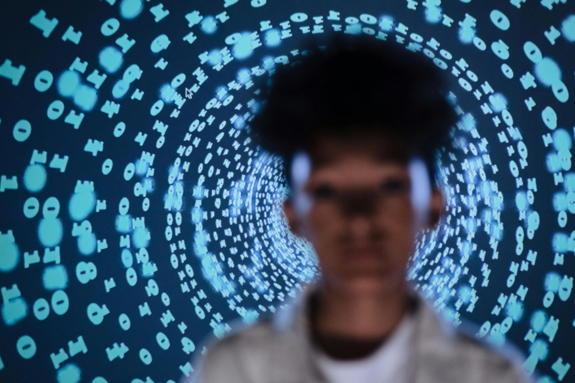 Blurred person in front of a tunnel of glowing blue symbols; could be a digital data visualization.