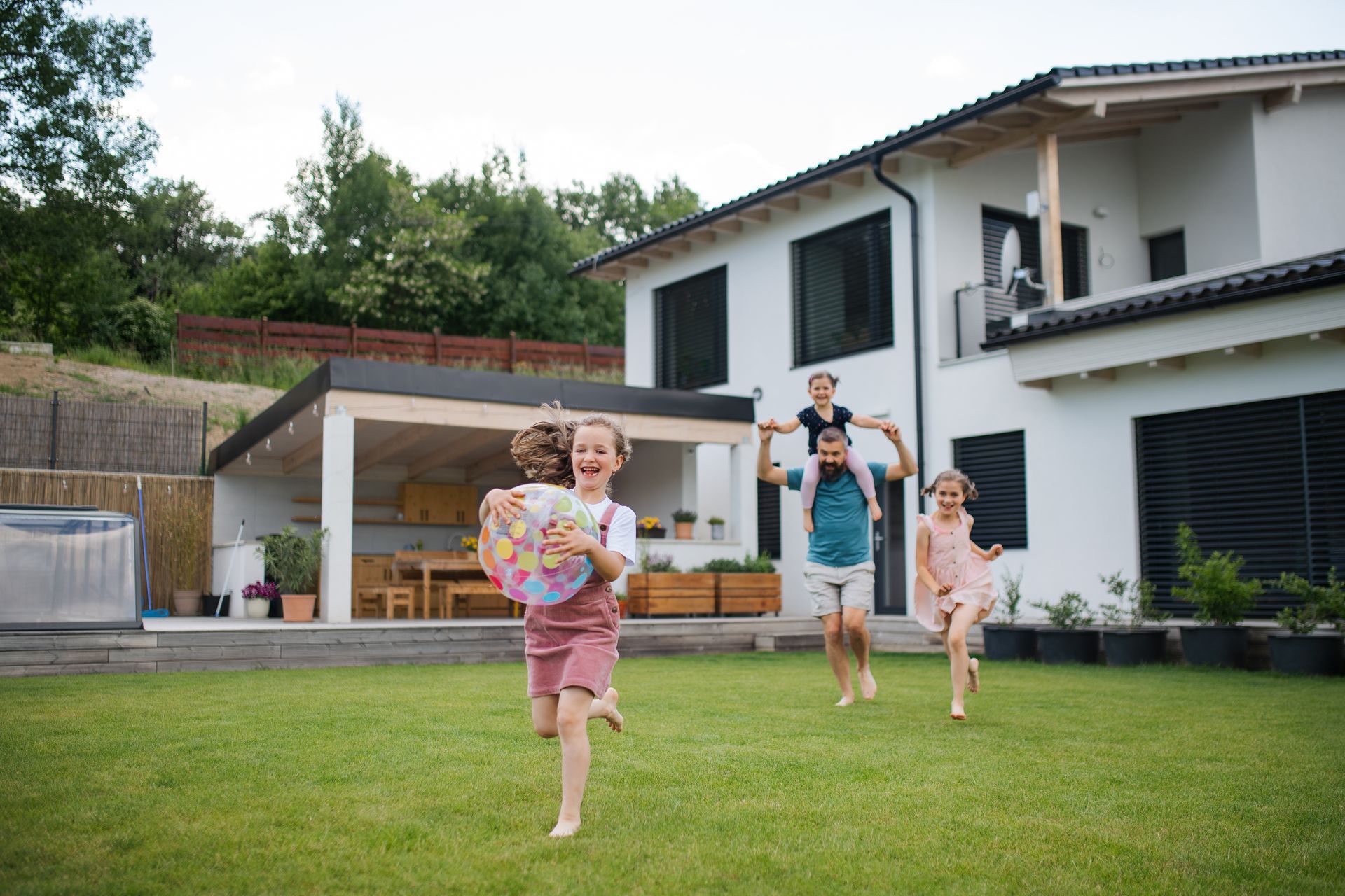 A family is sitting on the porch of their house next to a swimming pool.