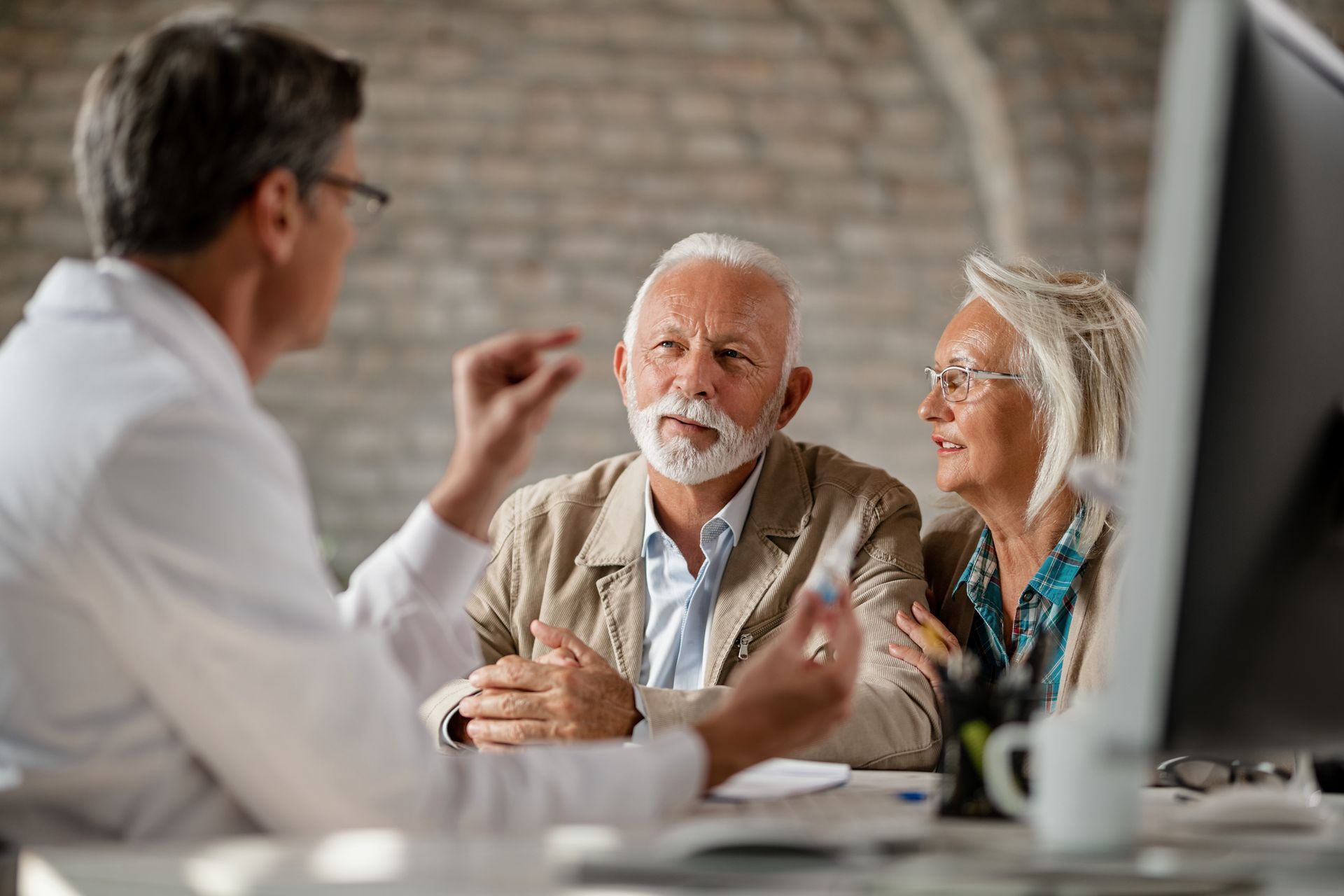 Doctor speaking to an older couple at a desk in an office setting.