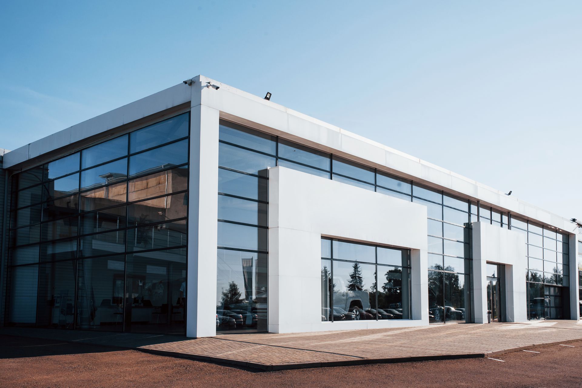 Modern white building with large glass windows reflecting the sky and surroundings, under a blue sky.