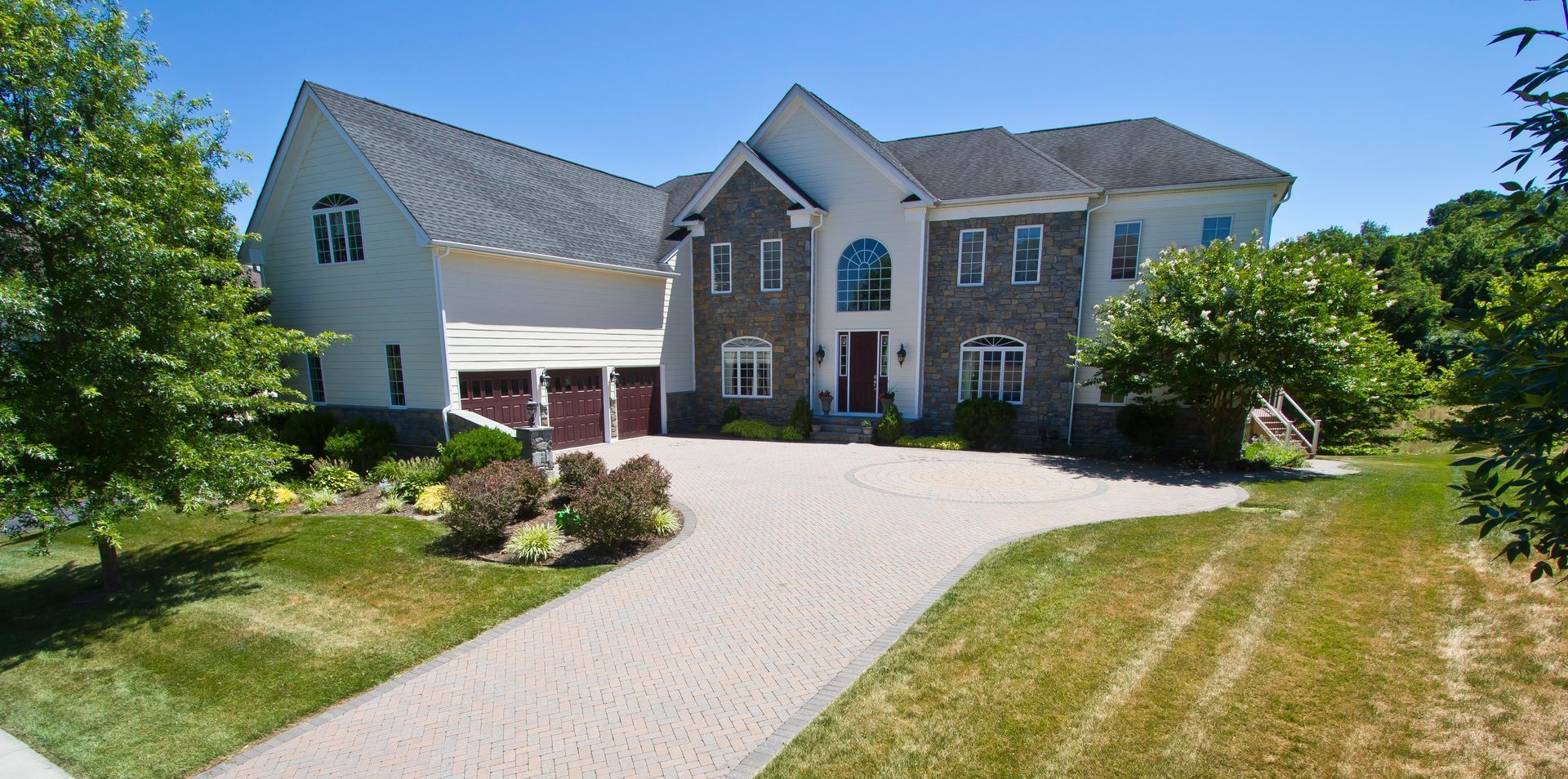 Large, multi-story house with stone facade, arched entryway, and brick driveway.