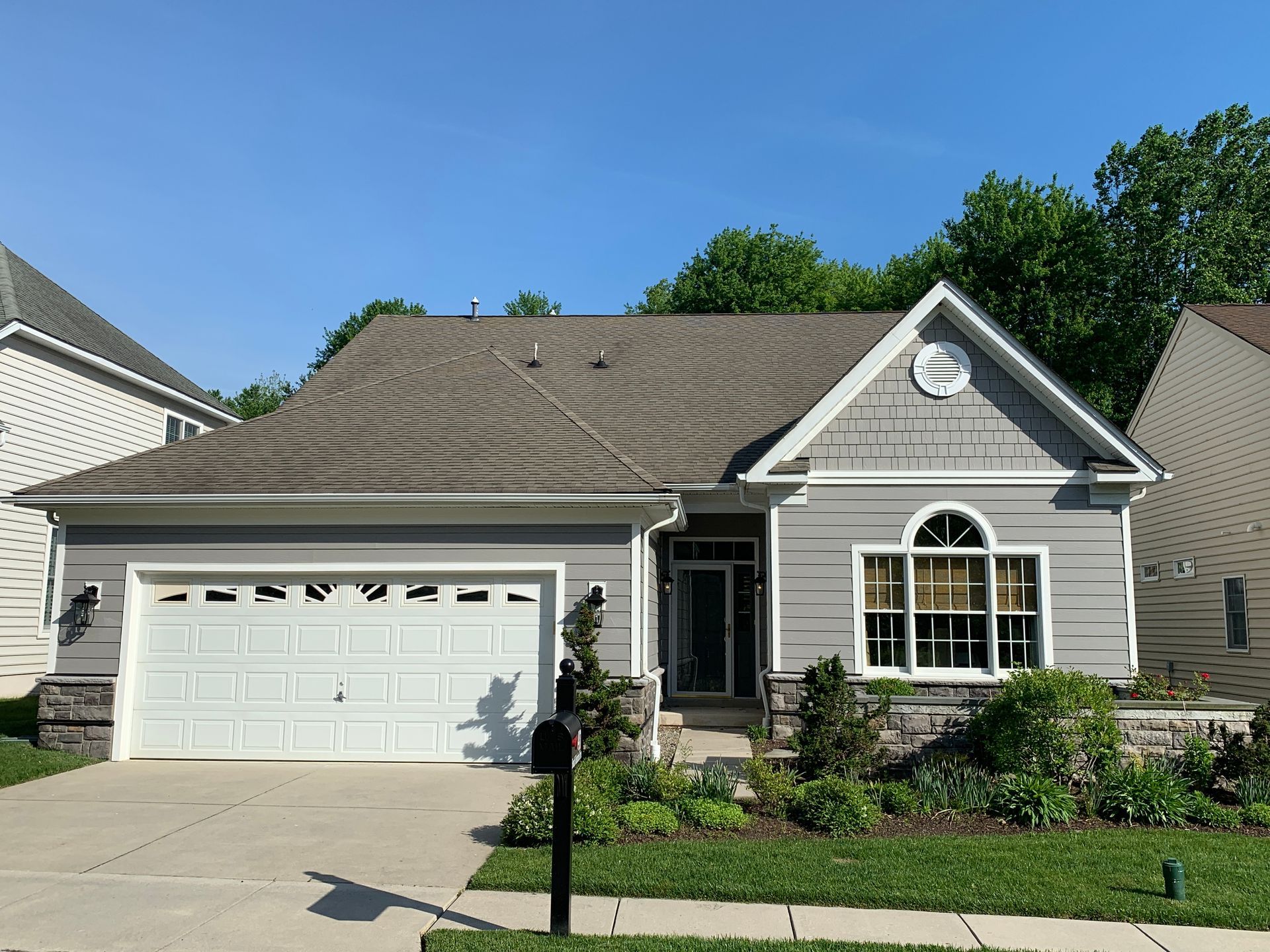 Gray house with white garage door, front landscaping, and blue sky.