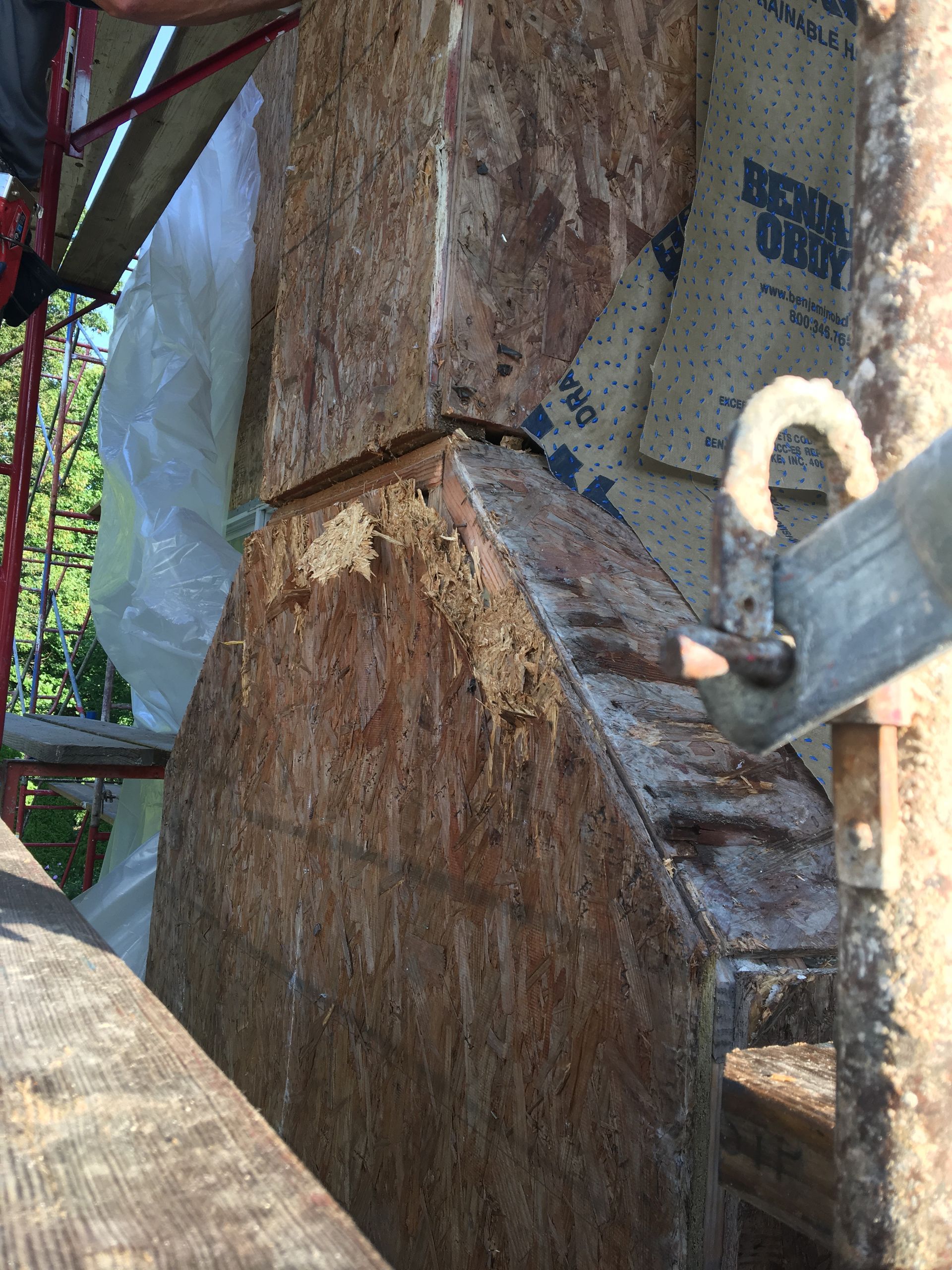 Wooden structure corner with damaged OSB and building wrap. Scaffolding is visible.