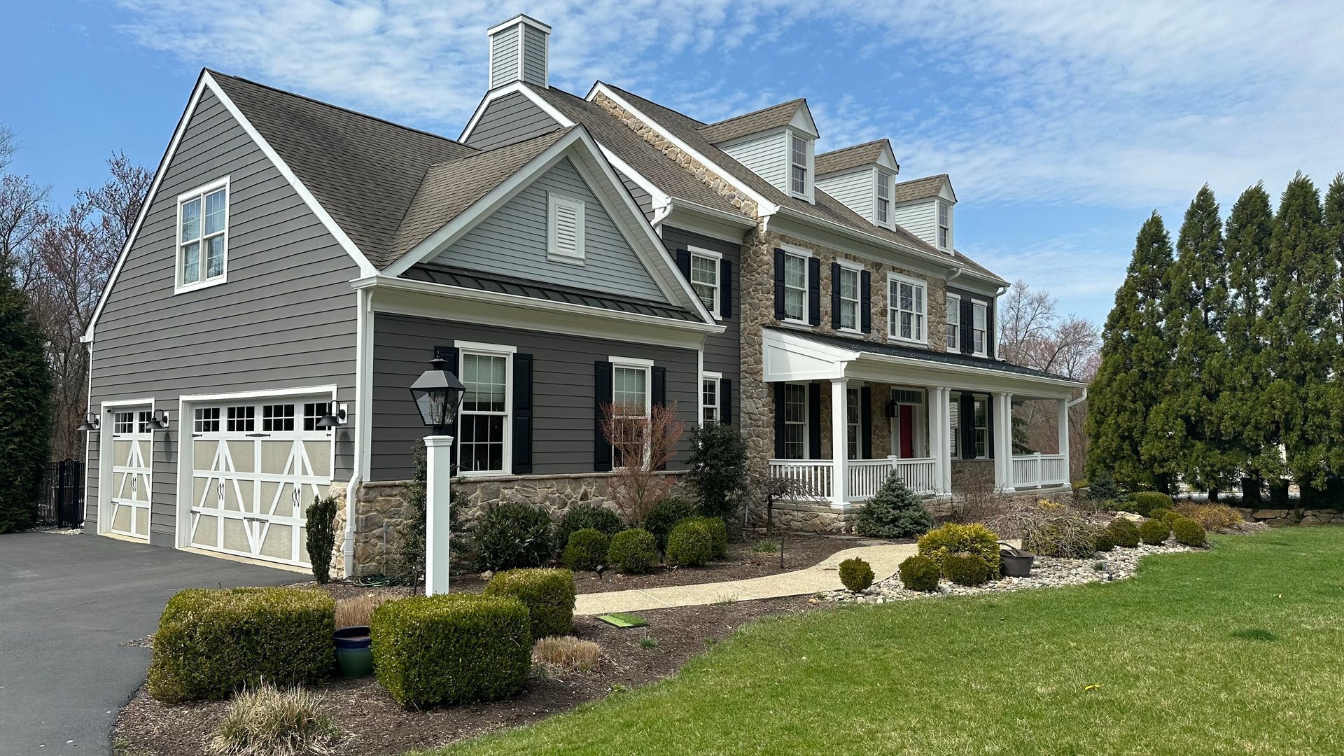 Two-story gray house with garage, porch, and lawn on a sunny day.