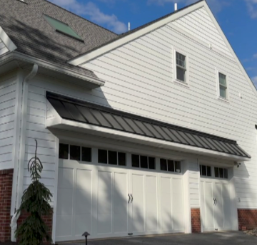 White house with white garage doors and black trim under a blue sky.