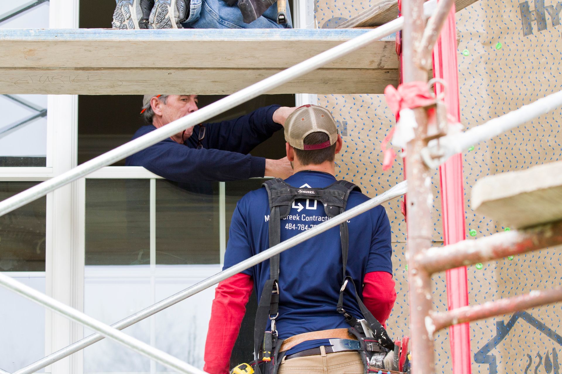 Two construction workers installing a window, one in the window frame and the other at scaffolding.