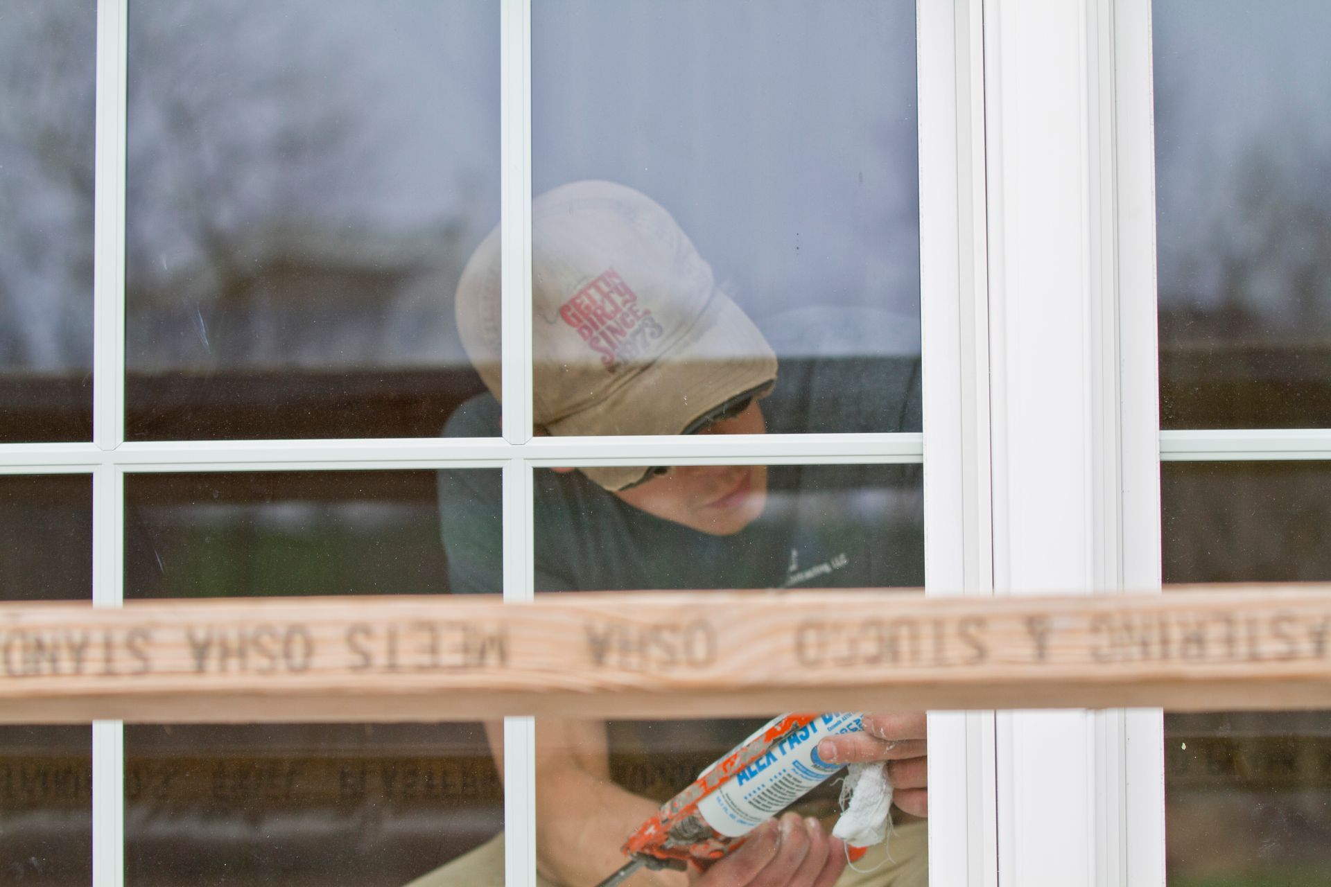 Person applying caulk to a window frame, viewed through the window.