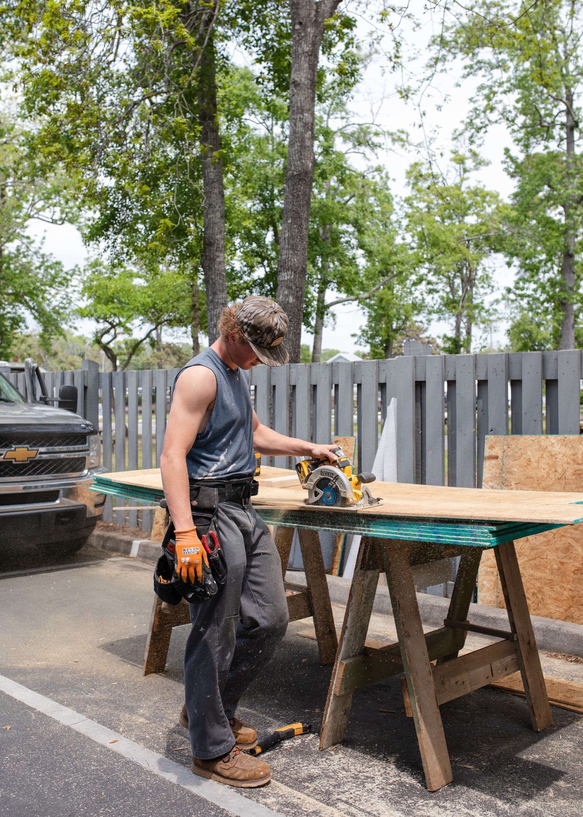Carpenter cuts wood with a circular saw outside. He wears work clothes and safety gear.
