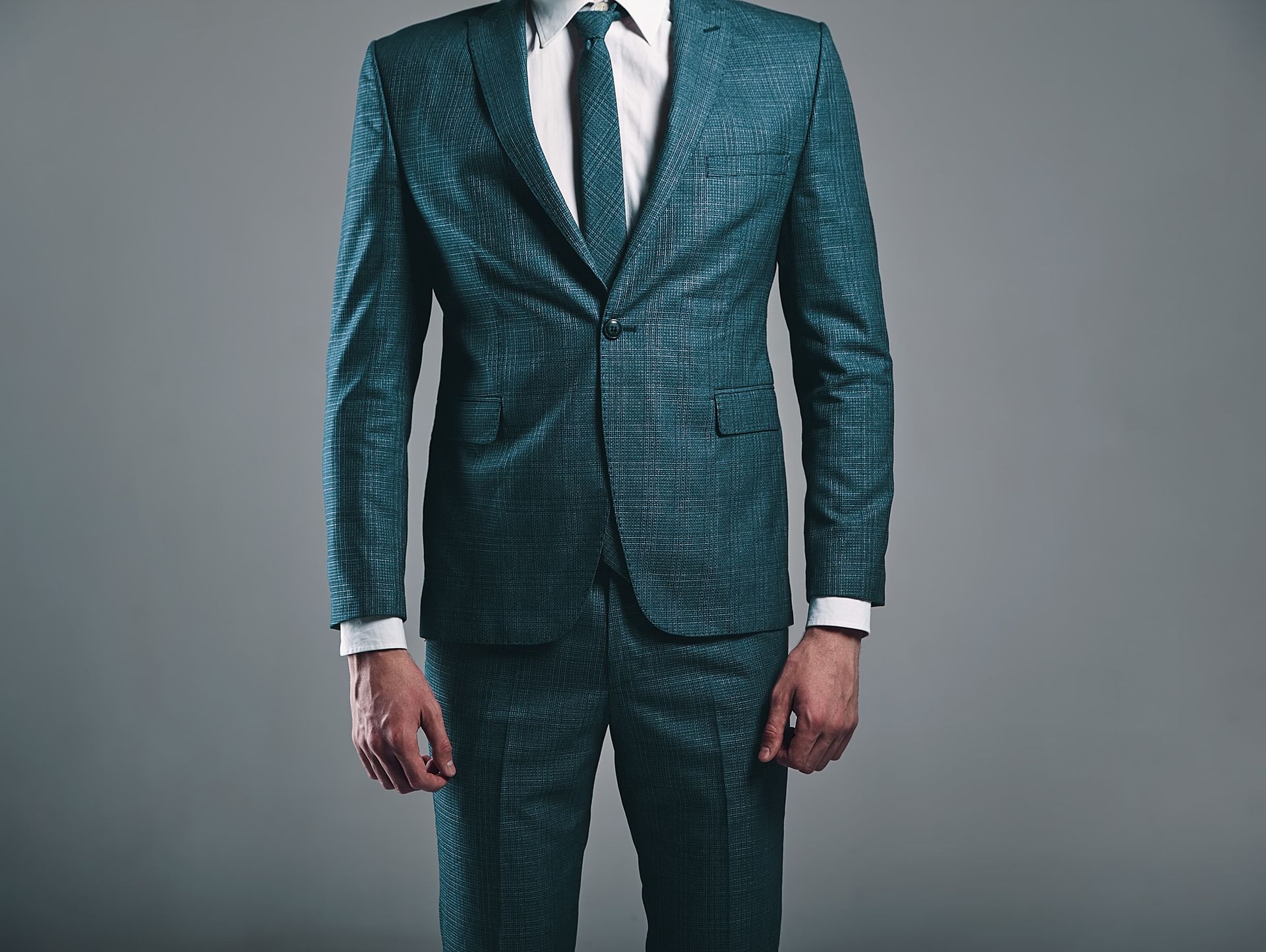 A man in a green suit and tie is standing in front of a gray background.