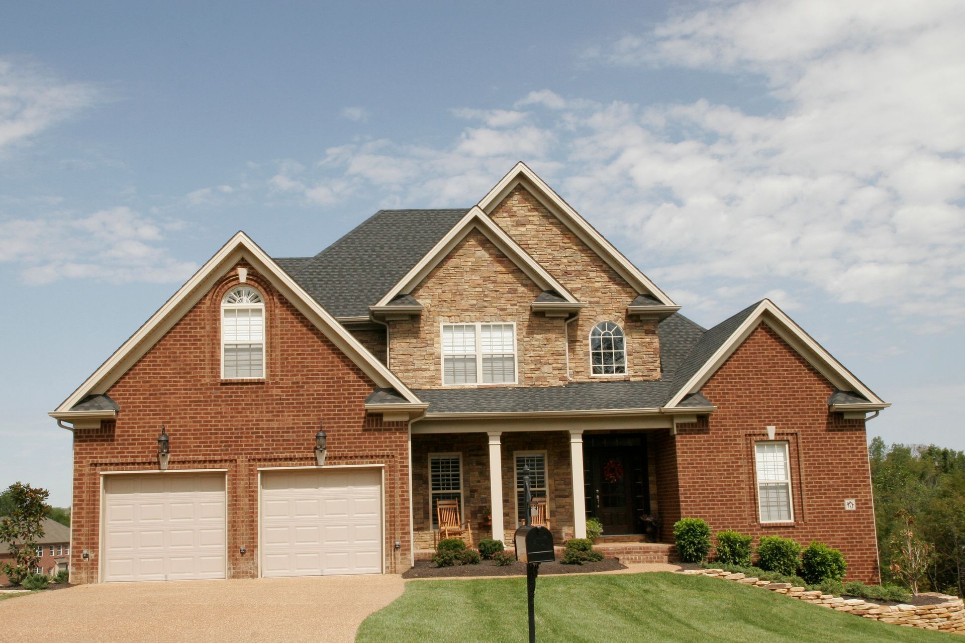 Two-story brick house with a brown roof and a two-car garage under a blue sky.