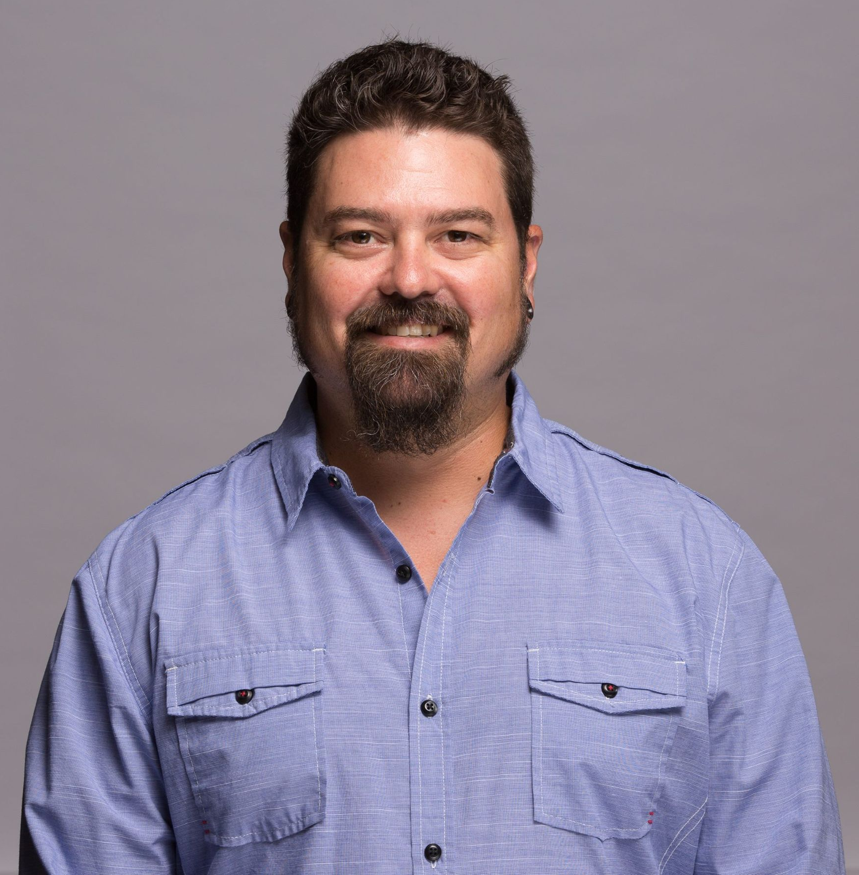 Smiling person in a light blue button-up shirt against a gray background