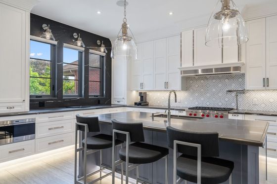 Modern white kitchen with black accents, island seating, pendant lights, and large window view