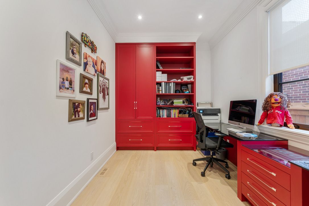 Modern home office with red cabinets, framed photos, desk, chair, and a stuffed toy by the window.