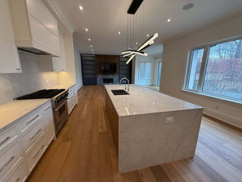 Modern kitchen with white cabinets, wood floors, marble island, and large windows looking outside