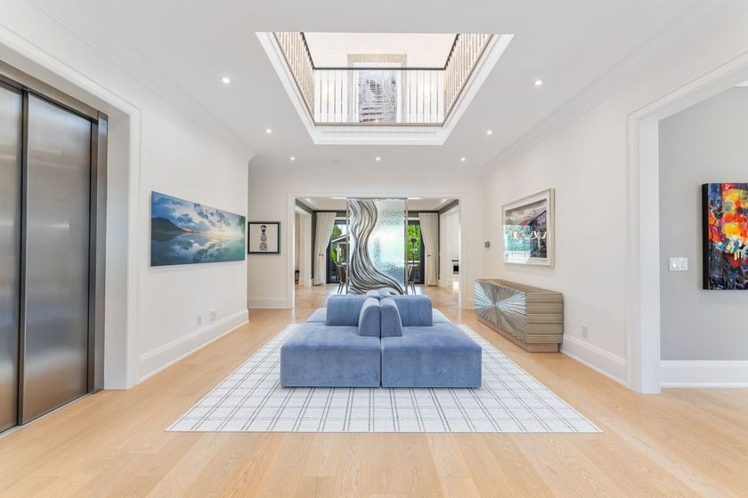 Bright modern living room with skylight, blue sofa, art on white walls, and elevator doors on the left