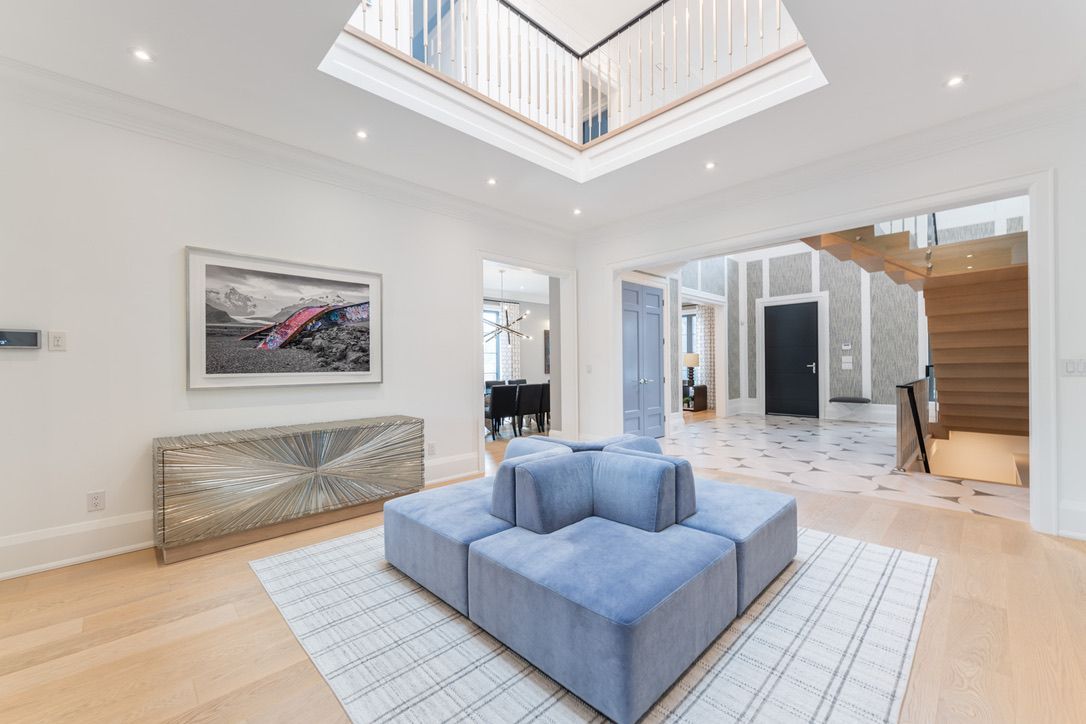 Bright modern living room with blue ottomans, white walls, skylight, and staircase at right
