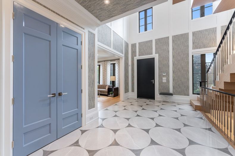 Bright modern lobby with blue double doors, patterned floor, tall windows, and staircase railing