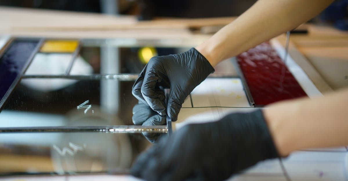 A person wearing black gloves is working on a piece of mirror.