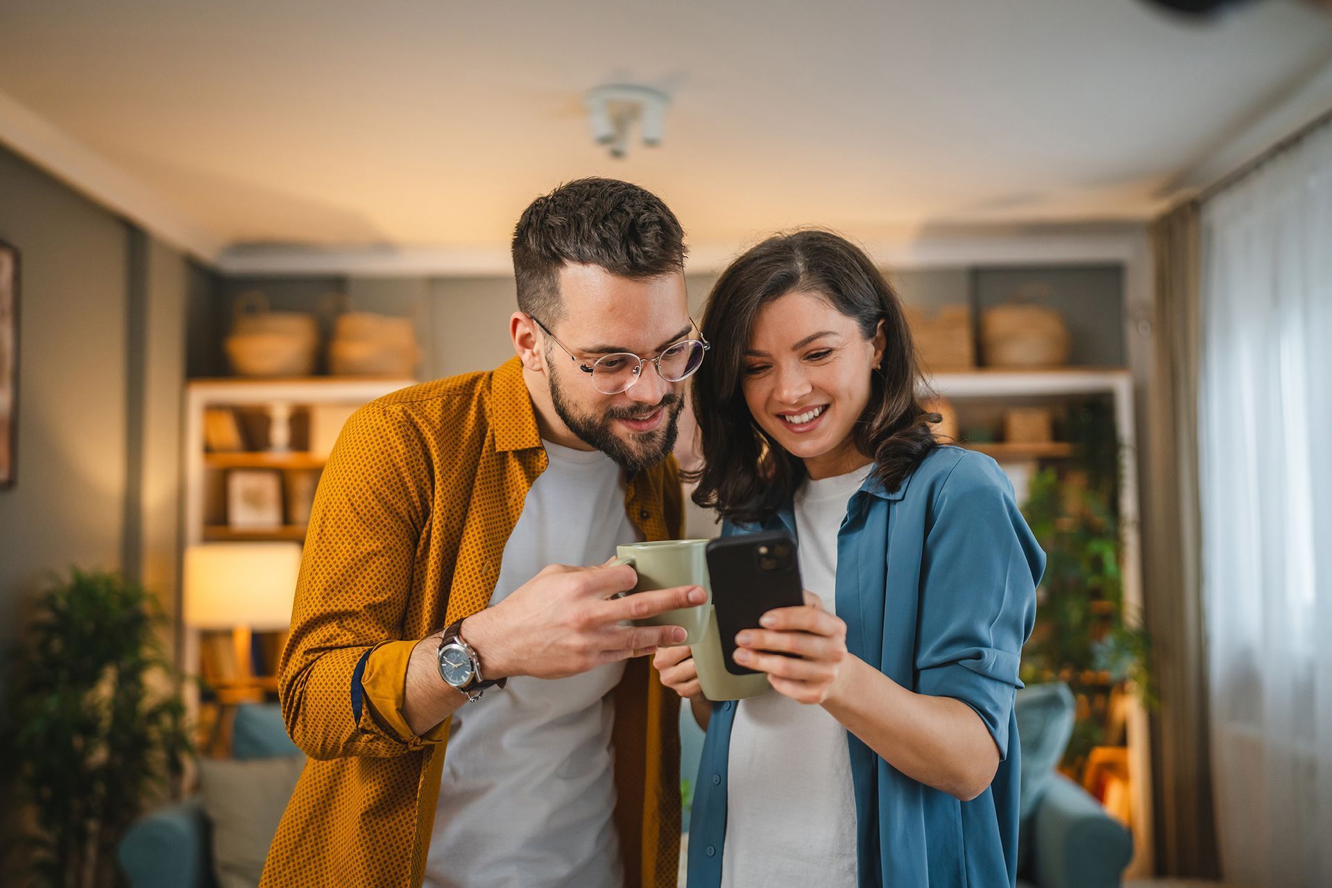 A man and a woman are looking at a cell phone in a living room.