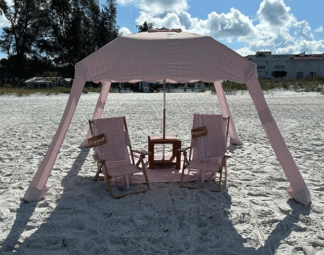 A pink tent with chairs and an umbrella on the beach