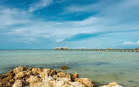 A pier in the middle of the ocean with rocks in the foreground.