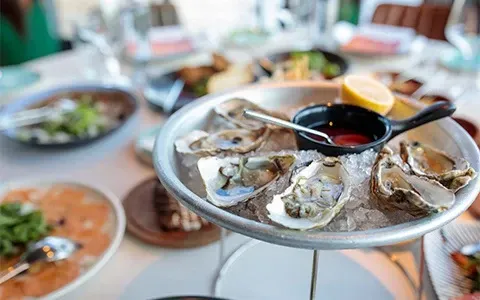 A plate of oysters on ice with sauce and a spoon on a table.