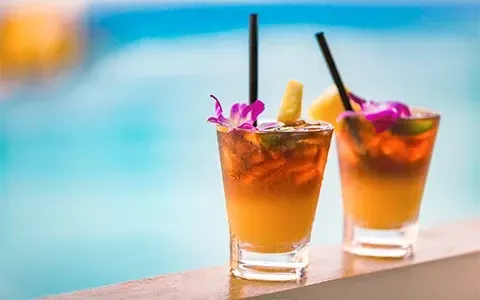Two cocktails are sitting on a ledge next to a pool.