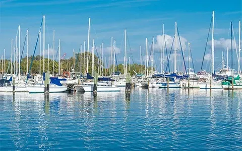 A row of sailboats are docked in a marina on a sunny day.