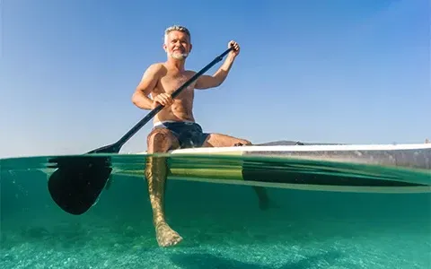 A man is sitting on a paddle board in the ocean.