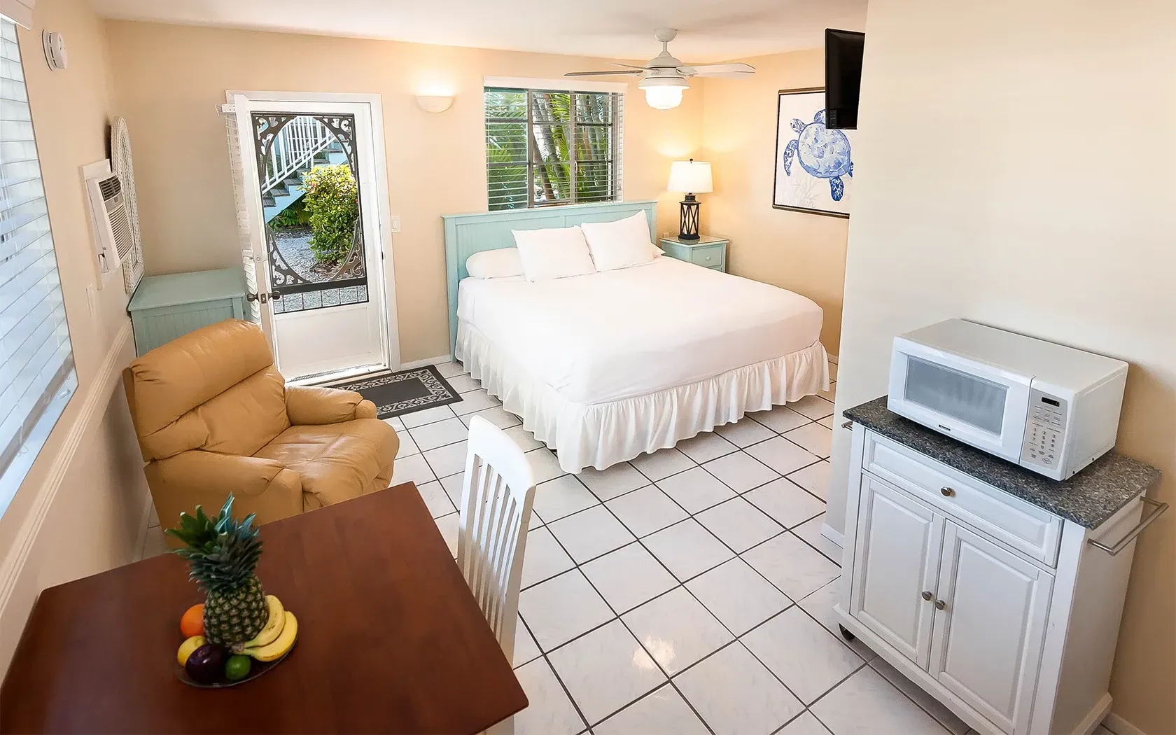 A hotel room with a king size bed , chair , table and microwave.