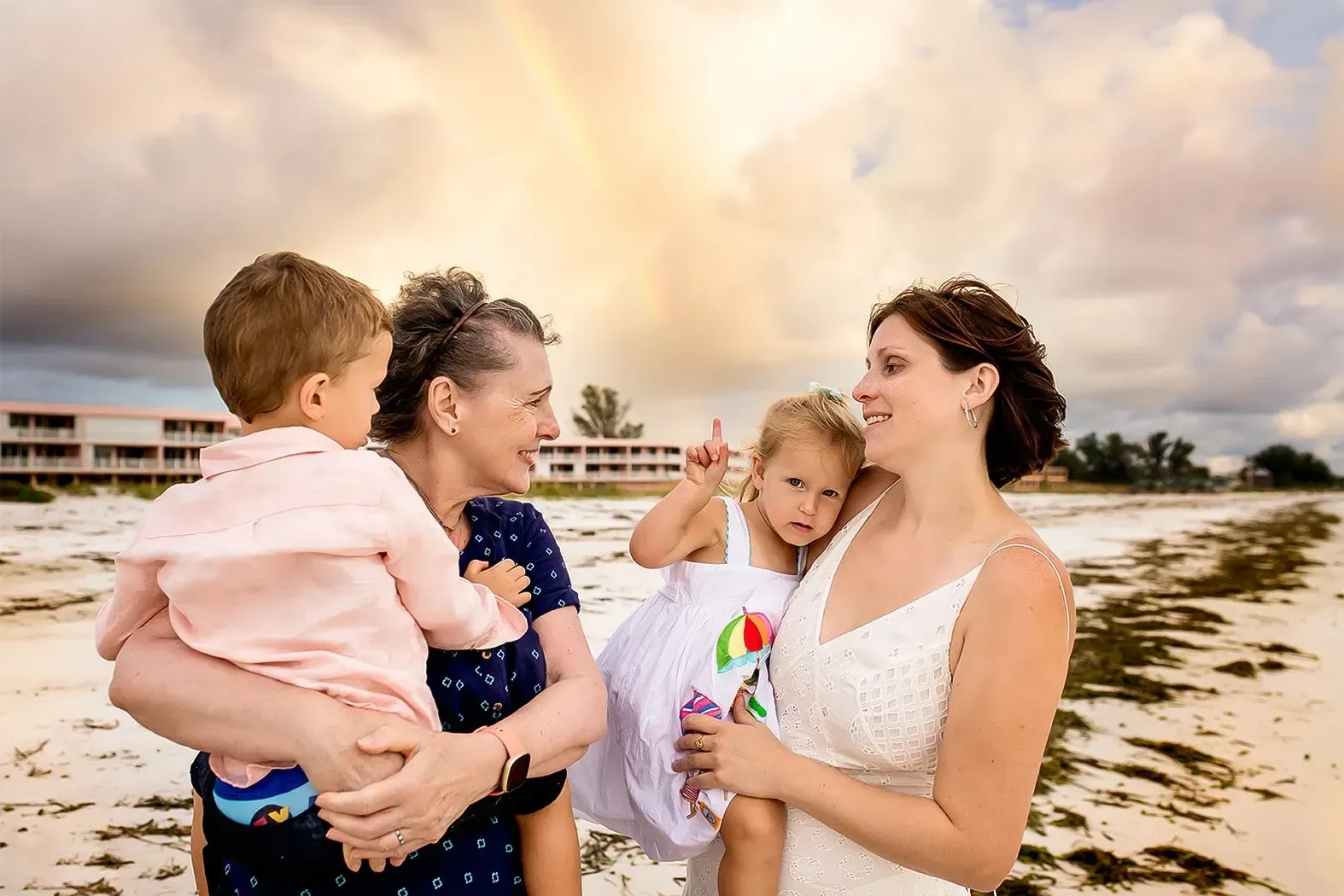 A bride and groom are holding two children on the beach.