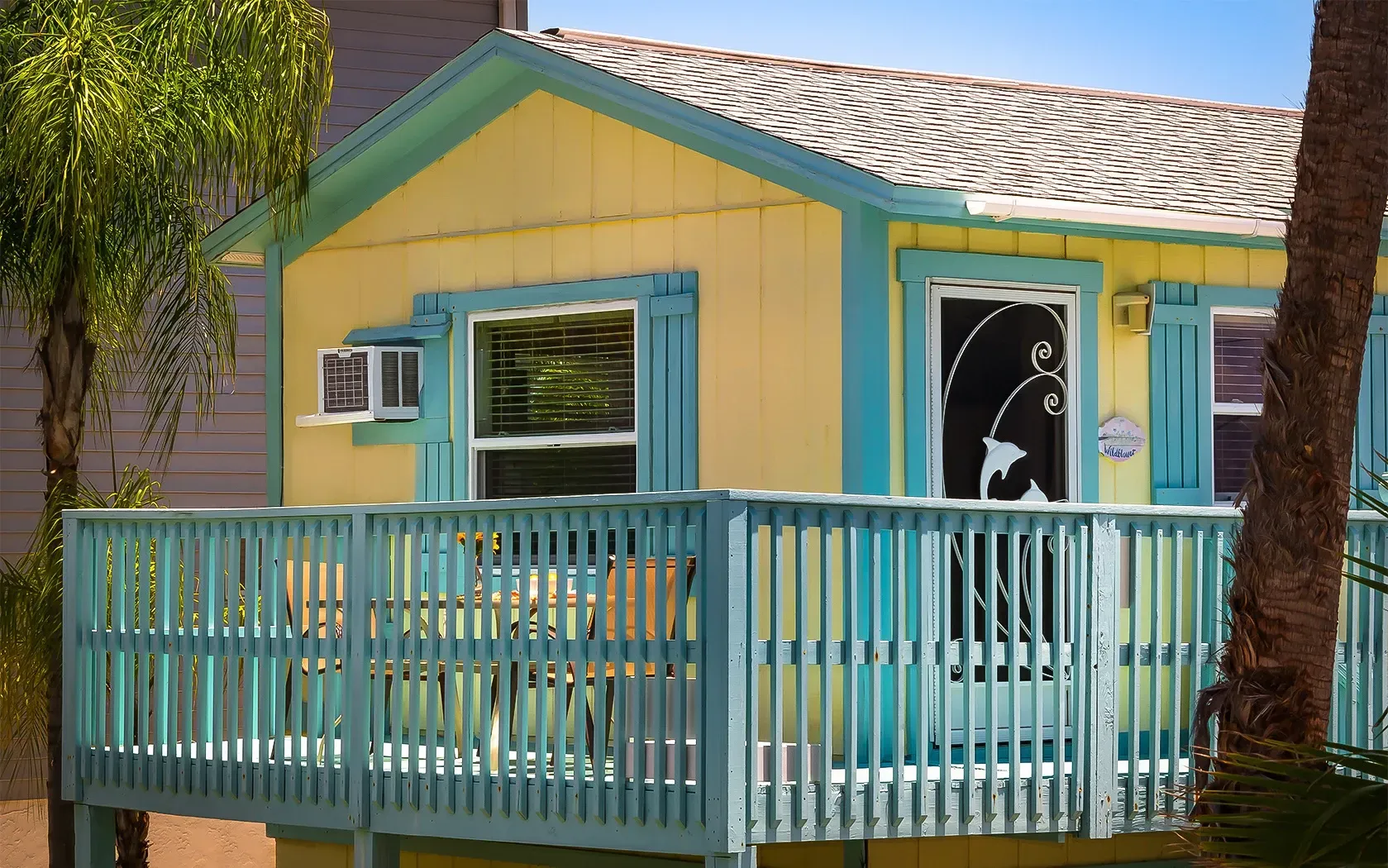 A small yellow and blue house with a blue deck.