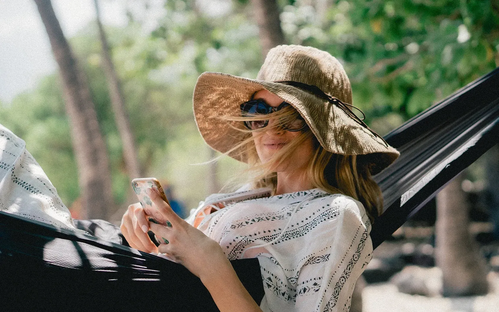 A woman is sitting in a hammock looking at her phone.
