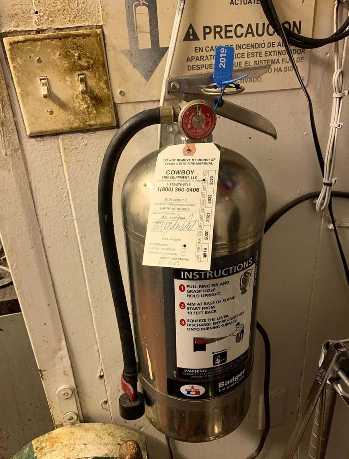 A metal fire extinguisher with instructions and a tag hanging in a room.