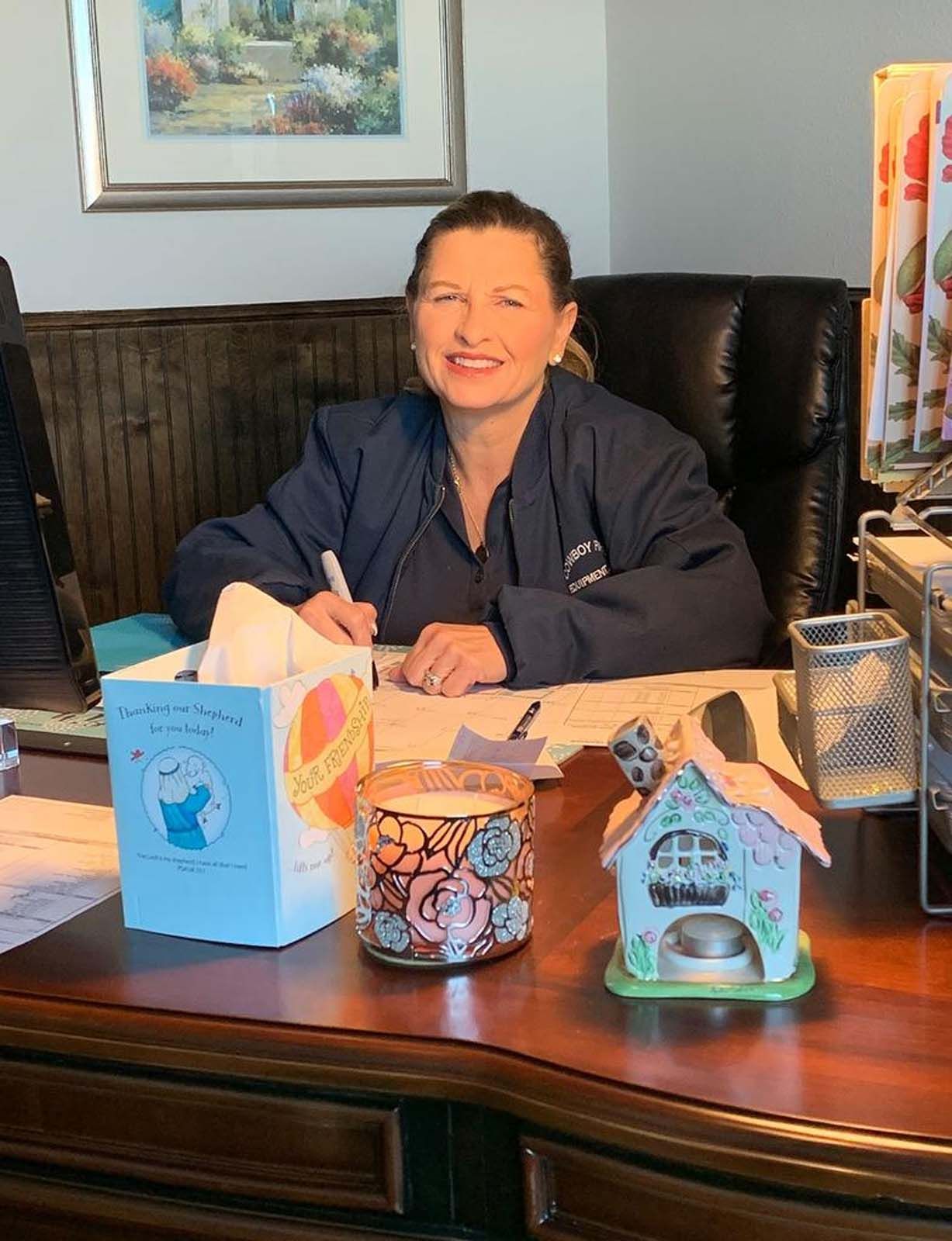 Woman in blue top seated at desk, writing.