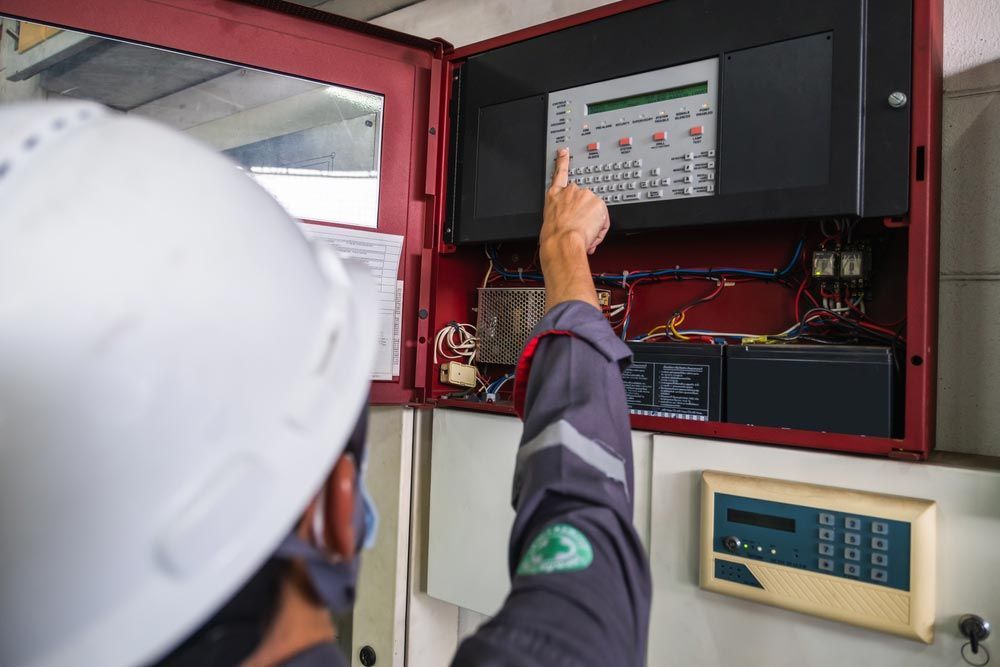 A Man Wearing a Hard Hat and a Mask is Working on a Fire Alarm System — Big Bang Electrical And Air In Trinity Park, QLD